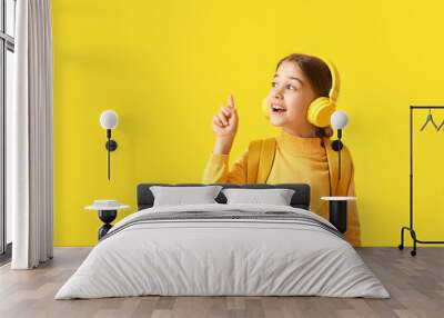 Cute little girl with headphones and raised index finger on color background Wall mural