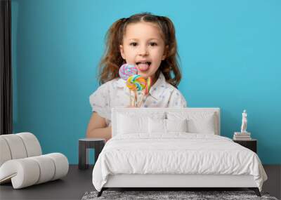 Cute little girl with lollipops showing tongue on blue background Wall mural