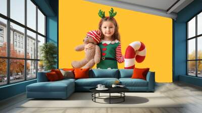 Cute little girl with teddy bear and Christmas cushion on color background Wall mural