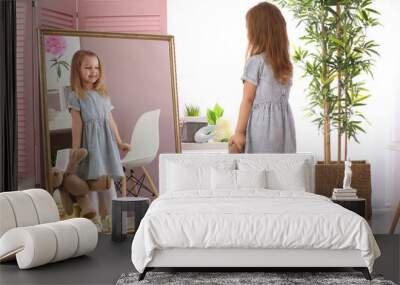 Cute little girl with teddy bear looking in mirror at home Wall mural