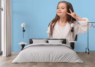 Cute little happy girl in bathrobe showing victory gesture on blue background Wall mural