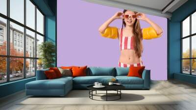 Cute little happy girl in swimsuit with inflatable armbands on purple background Wall mural