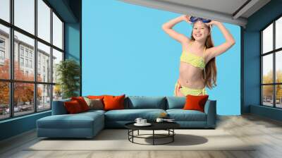 Cute little happy girl in swimsuit with snorkeling mask on blue background Wall mural