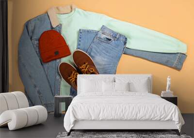 Denim jacket, sweater, jeans, hat and shoes on color background Wall mural