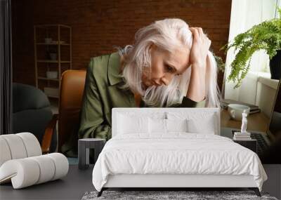 Depressed mature woman sitting near table at home Wall mural