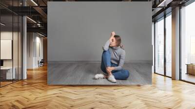 Depressed young woman sitting on floor near grey wall Wall mural