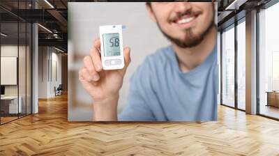 Diabetic young man using glucometer at home, closeup Wall mural