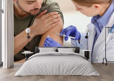 Doctor vaccinating young man in clinic Wall mural