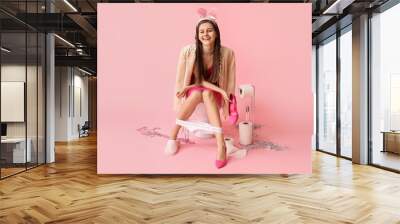 Drunk young woman sitting on toilet bowl after party against pink background Wall mural