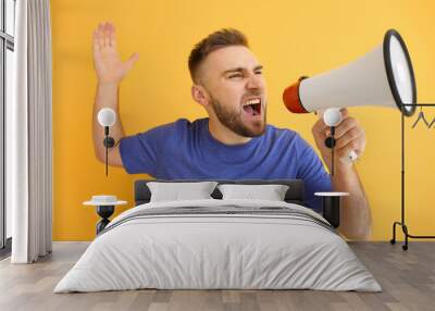 Emotional young man with megaphone on color background Wall mural