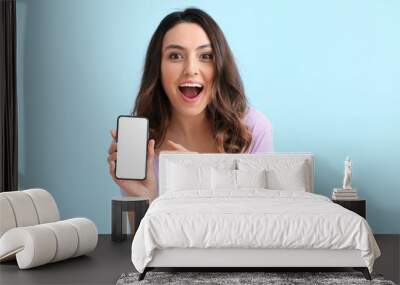 Excited young woman with mobile phone on blue background Wall mural