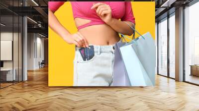 Fashionable young Asian woman in stylish denim shorts with shopping bags and credit cards on yellow background Wall mural