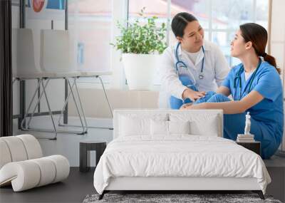 Female Asian doctor calming her colleague in clinic Wall mural