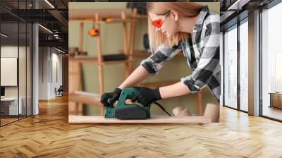 Female carpenter smoothing wooden plank in workshop Wall mural