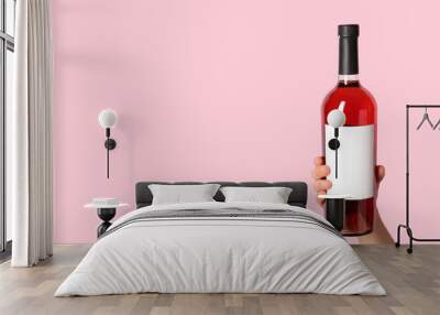 Female hand holding bottle of red wine on pink background Wall mural