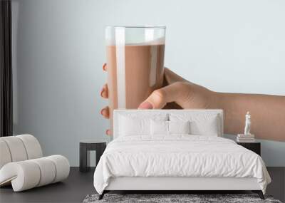 Female hand holding glass of delicious chocolate milk on grey background Wall mural