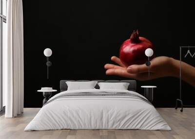 Female hand with ripe pomegranate on dark background Wall mural