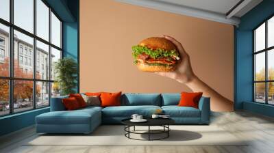 Female hand with tasty burger on color background Wall mural