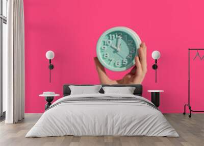 Female hands holding alarm clock through hole on color background Wall mural