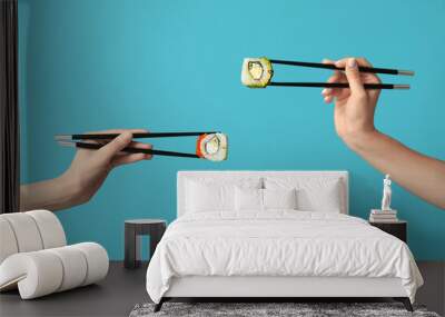 Female hands holding chopsticks with different tasty sushi rolls on blue background Wall mural