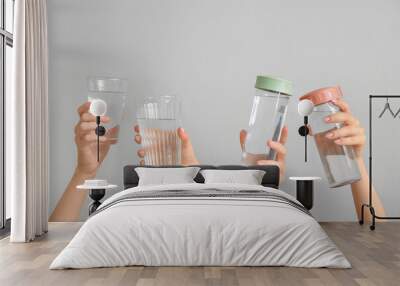 Female hands with bottles and glasses of cold water on light background Wall mural