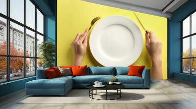 Female hands with cutlery and empty plate on color background Wall mural