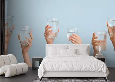 Female hands with glasses of water on light blue background Wall mural