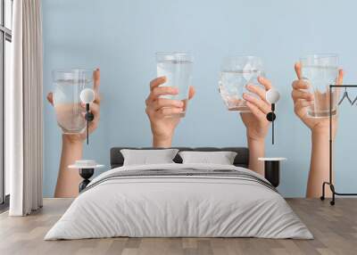 Female hands with glasses of water on light blue background Wall mural