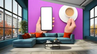 Female hands with mobile phone and cup of coffee on color background Wall mural