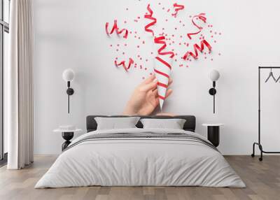 Female hands with party popper and confetti on light background Wall mural