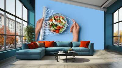 Female hands wrapping bowl with salad by stretch wrap on blue background Wall mural