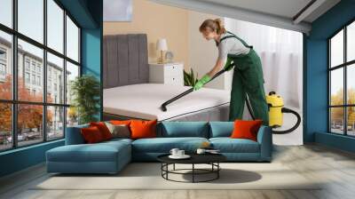 Female janitor cleaning mattress with vacuum cleaner in bedroom Wall mural