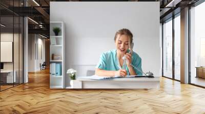 Female medical intern talking by telephone at reception in clinic Wall mural