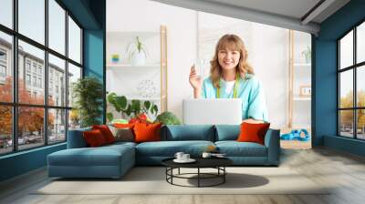 Female nutritionist with glass of water at table in kitchen Wall mural