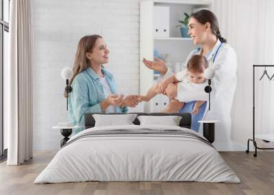 Female pediatrician with little baby talking to mother in clinic Wall mural