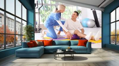 Female physiotherapist and young man with foam roller training in rehabilitation center Wall mural