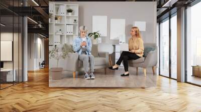 Female psychologist with teenage girl in headphones using mobile phone in office Wall mural