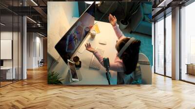 Female student with headphones playing video game on stream at home in evening Wall mural