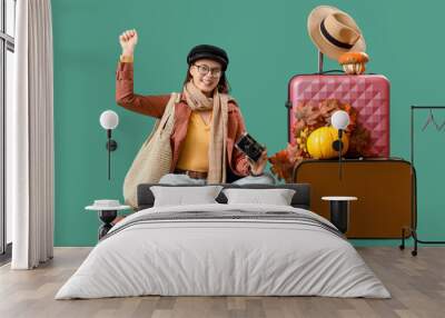 Female tourist in autumn clothes with photo camera and suitcases sitting on green background Wall mural