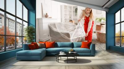 Female worker wrapping sofa with stretch film in room Wall mural