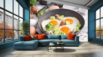 Frying pan with cooked eggs and vegetables on table Wall mural