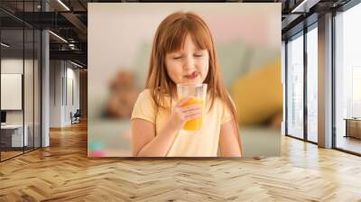 Funny little girl drinking citrus juice at home Wall mural