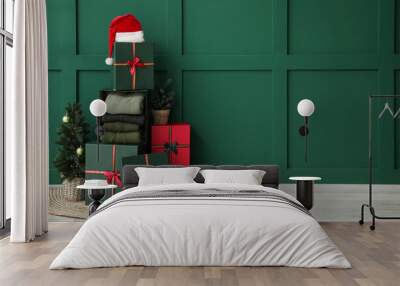 Gift boxes with winter sweaters and Christmas tree near green wall in room Wall mural