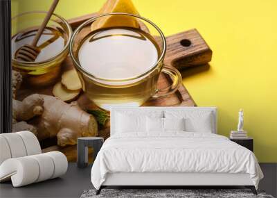 Glass cup of ginger tea and bowl with honey on yellow background Wall mural