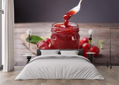 Glass jar and spoon with delicious strawberry jam on wooden table Wall mural