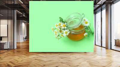 Glass jar of honey and fresh chamomile flowers on green background Wall mural