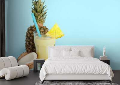 Glass of tasty pineapple smoothie, straw and coconut on blue background Wall mural