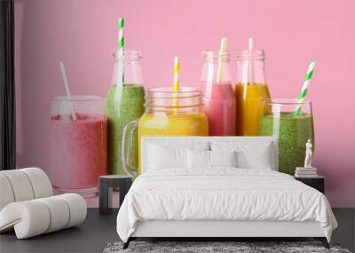 Glasses and bottles of different tasty smoothie with straws on pink background Wall mural