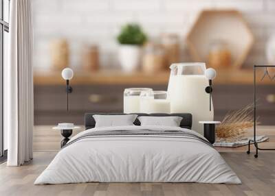 Glasses and jug of fresh milk with wheat ears on wooden table in kitchen Wall mural