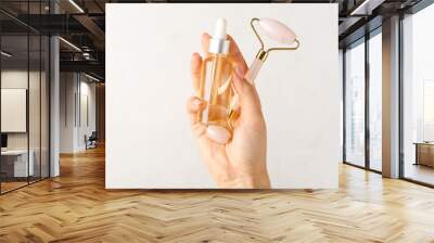 Hand with essential oil and facial massage tool on light background Wall mural